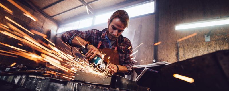 A person grinding metal, sparks flying, in a workshop setting.