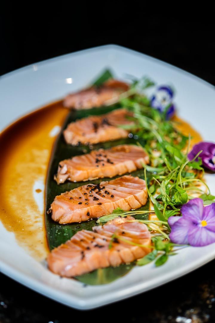 A white plate topped with slices of salmon and purple flowers.