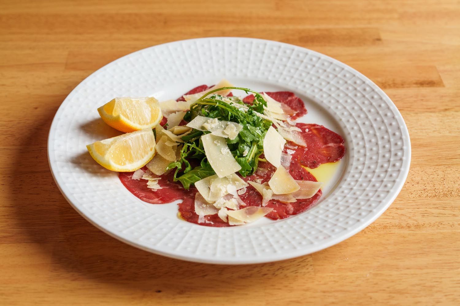 A white plate topped with meat and vegetables on a wooden table.