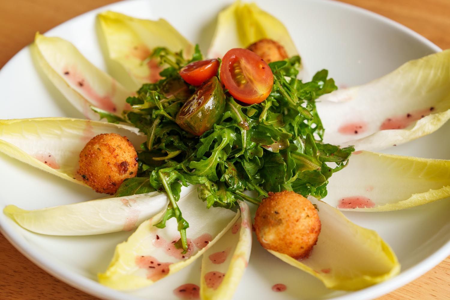 A white plate topped with salad and tomatoes on a wooden table.