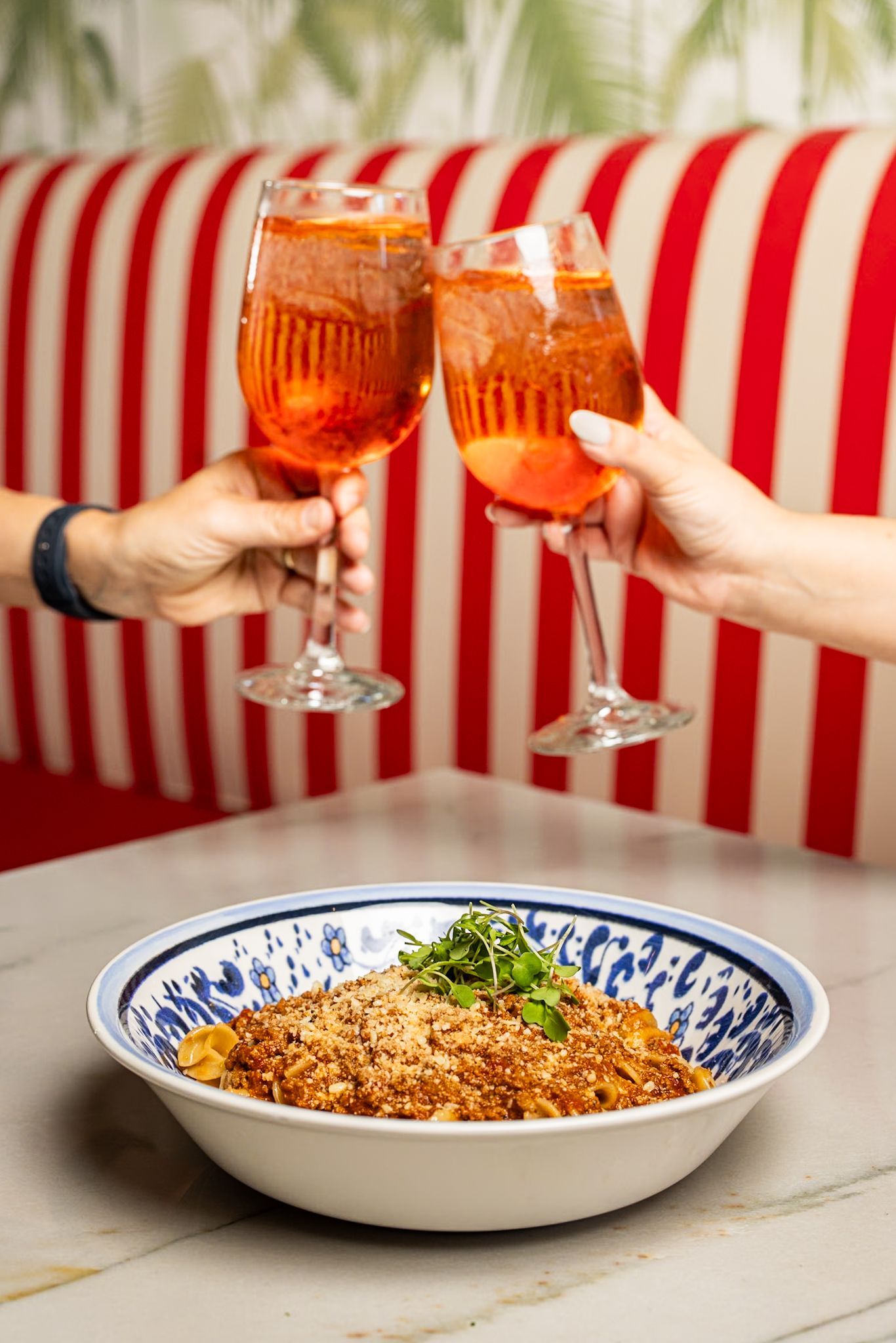 Two people are toasting with wine glasses in front of a bowl of food.