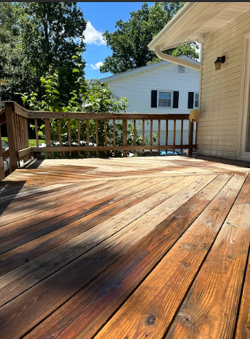 A wooden deck with a railing and a white house in the background.