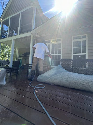 A man is cleaning a rug on a deck with a hose.