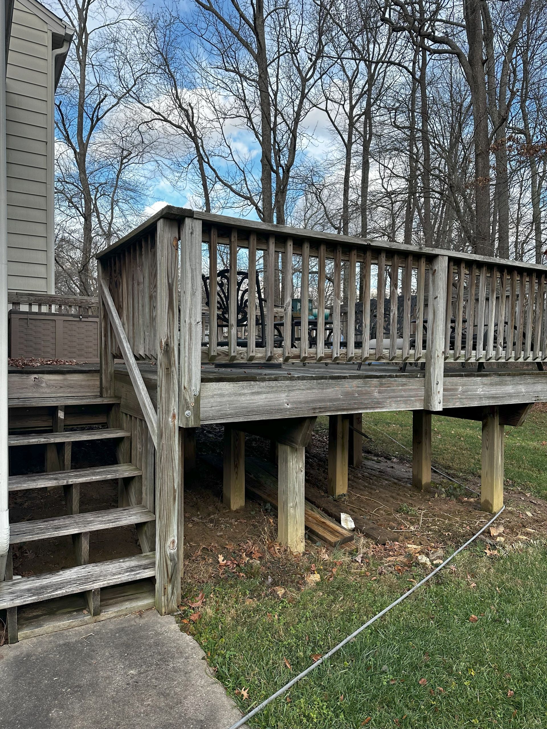 A wooden deck with stairs leading up to it is in the backyard of a house.