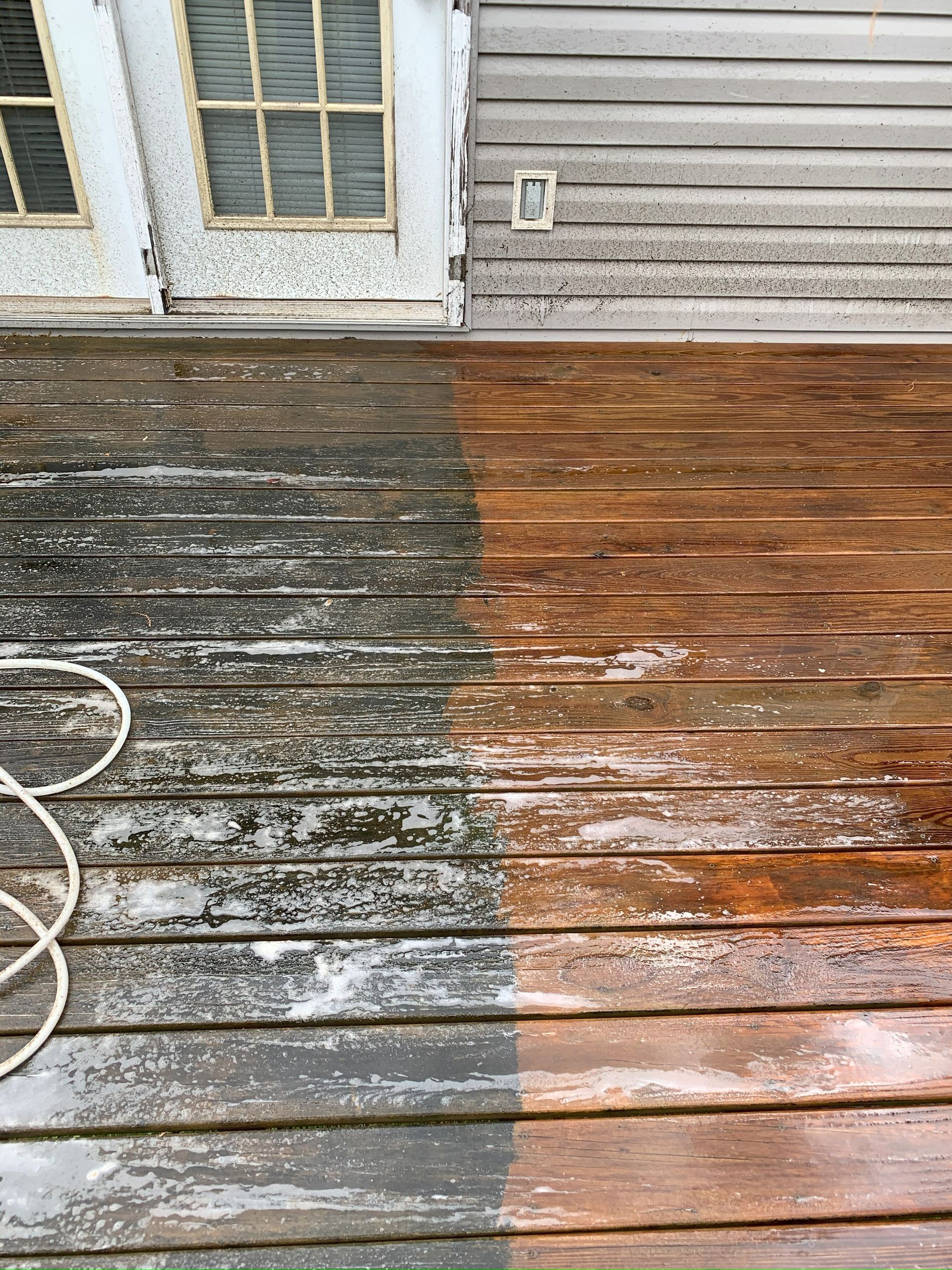 A before and after picture of a wooden deck being cleaned with a pressure washer.