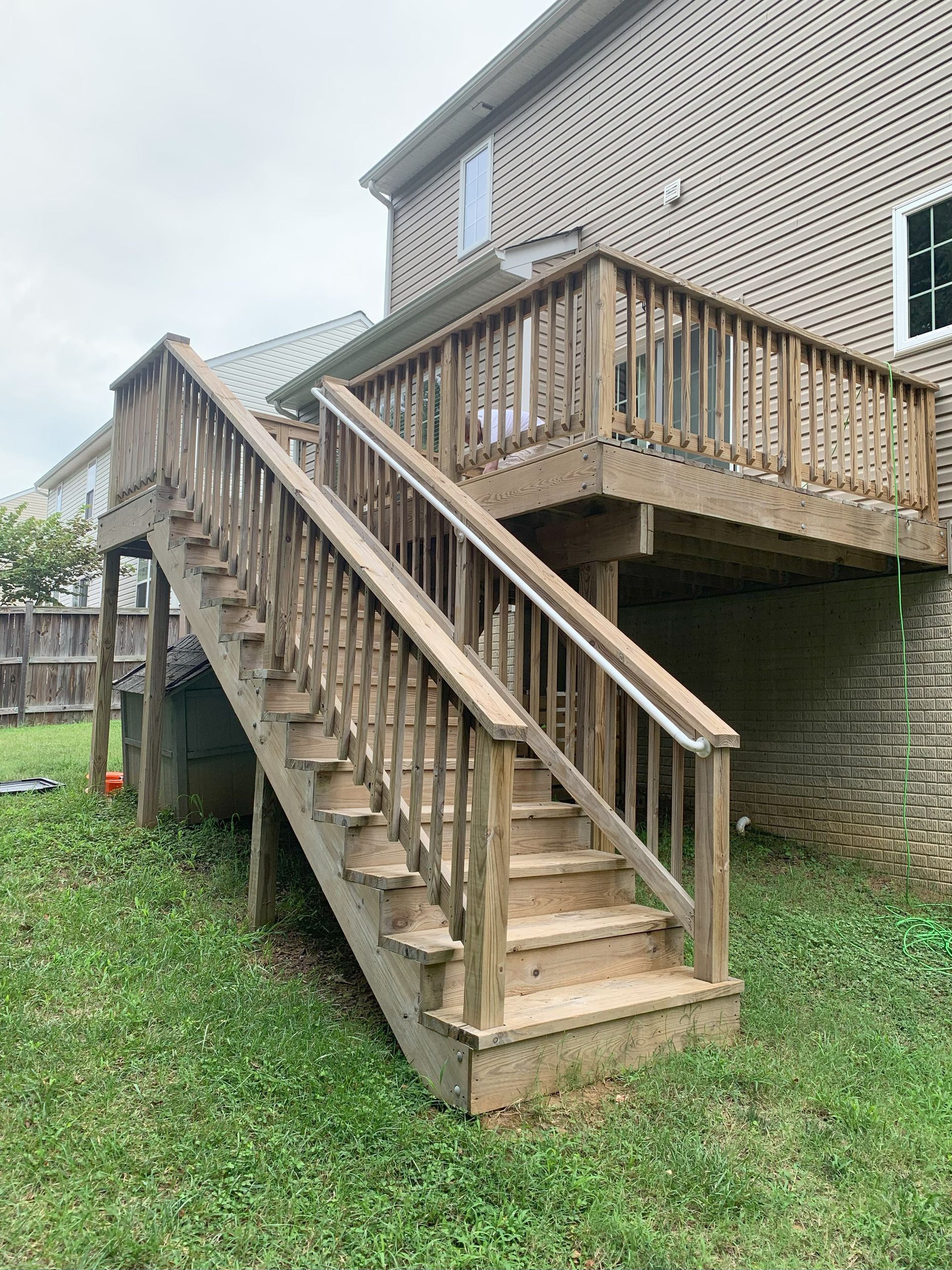 A wooden deck with stairs leading up to it is in the backyard of a house.