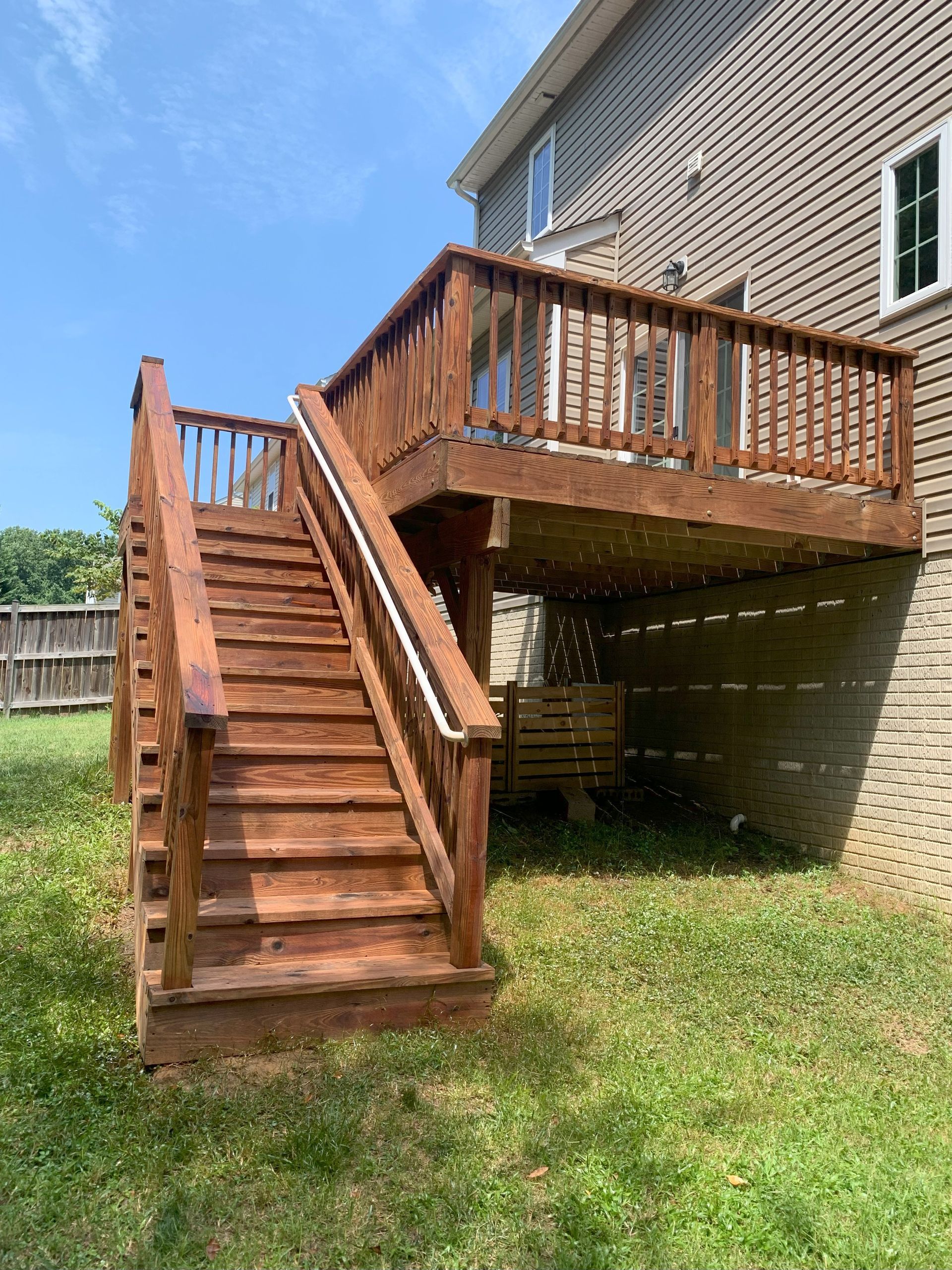 A wooden deck with stairs leading up to it is in the backyard of a house.