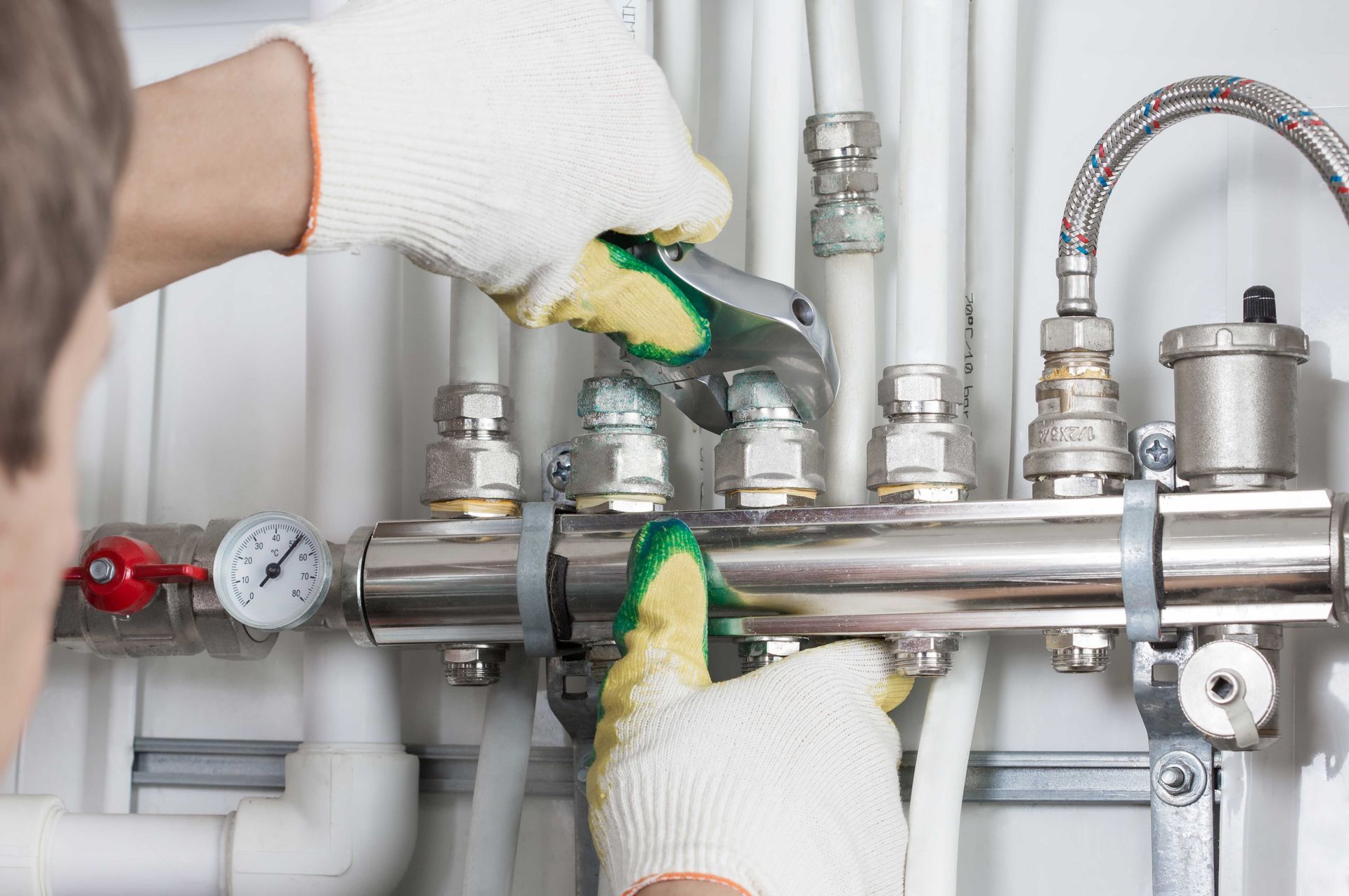 Hands wearing gloves tighten a pipe fitting with a wrench on a plumbing system. Hands wearing gloves tighten a pipe fitting with a wrench on a plumbing system.