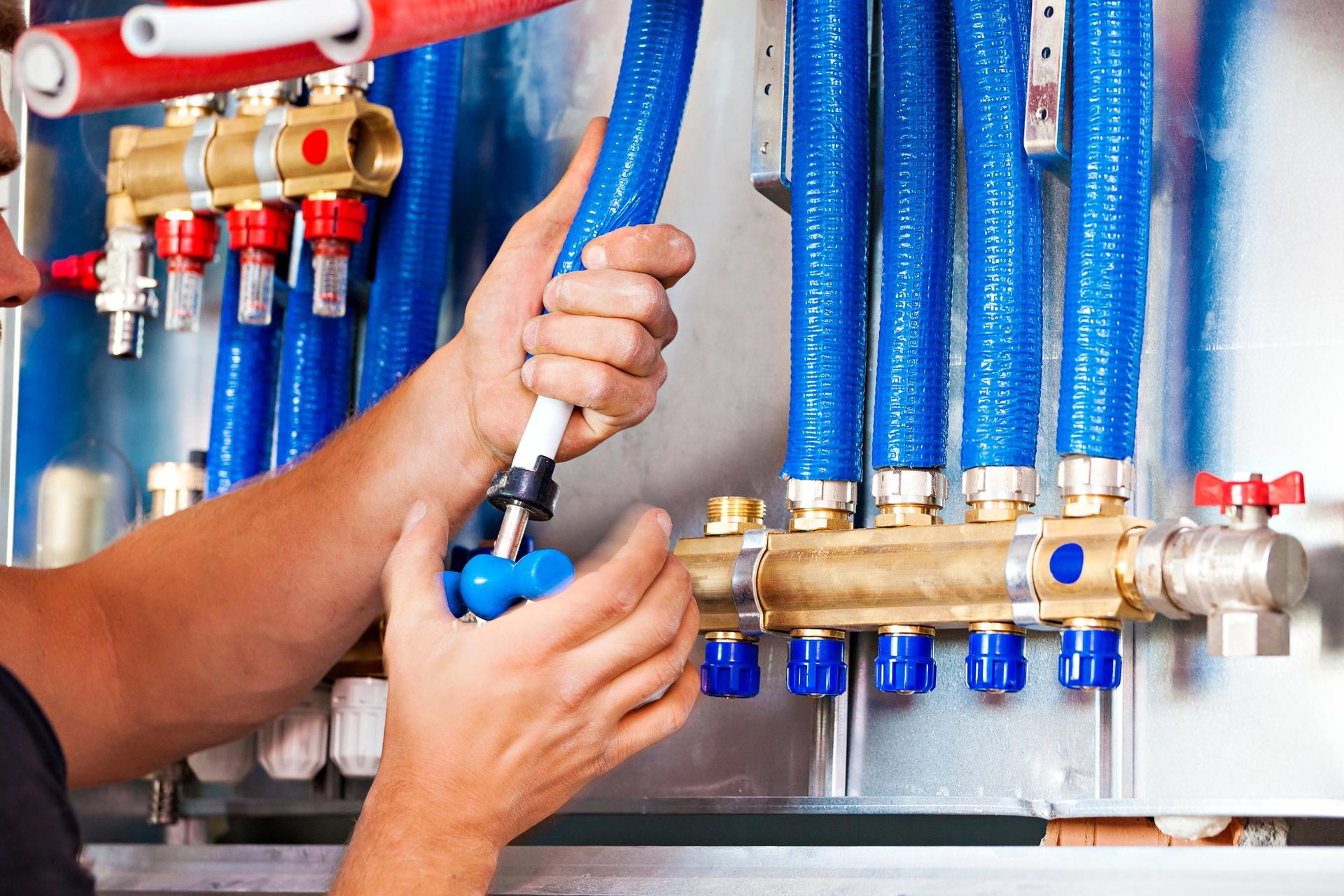 Plumber connecting blue pipe to brass manifold with red and blue valve controls. Plumber connecting blue pipe to brass manifold with red and blue valve controls.