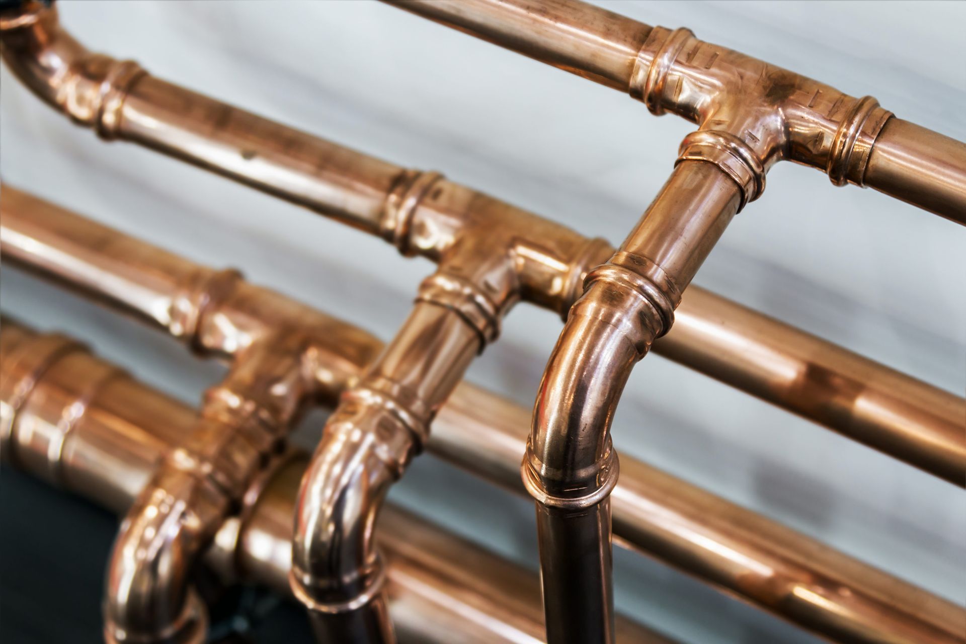 Copper plumbing pipes and joints, with curves and T-shapes, against a light gray wall. Copper plumbing pipes and joints, with curves and T-shapes, against a light gray wall.