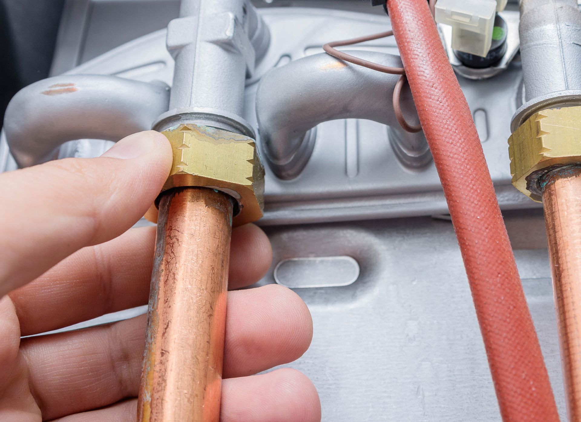 Hand tightening brass nut on copper pipe near a boiler.