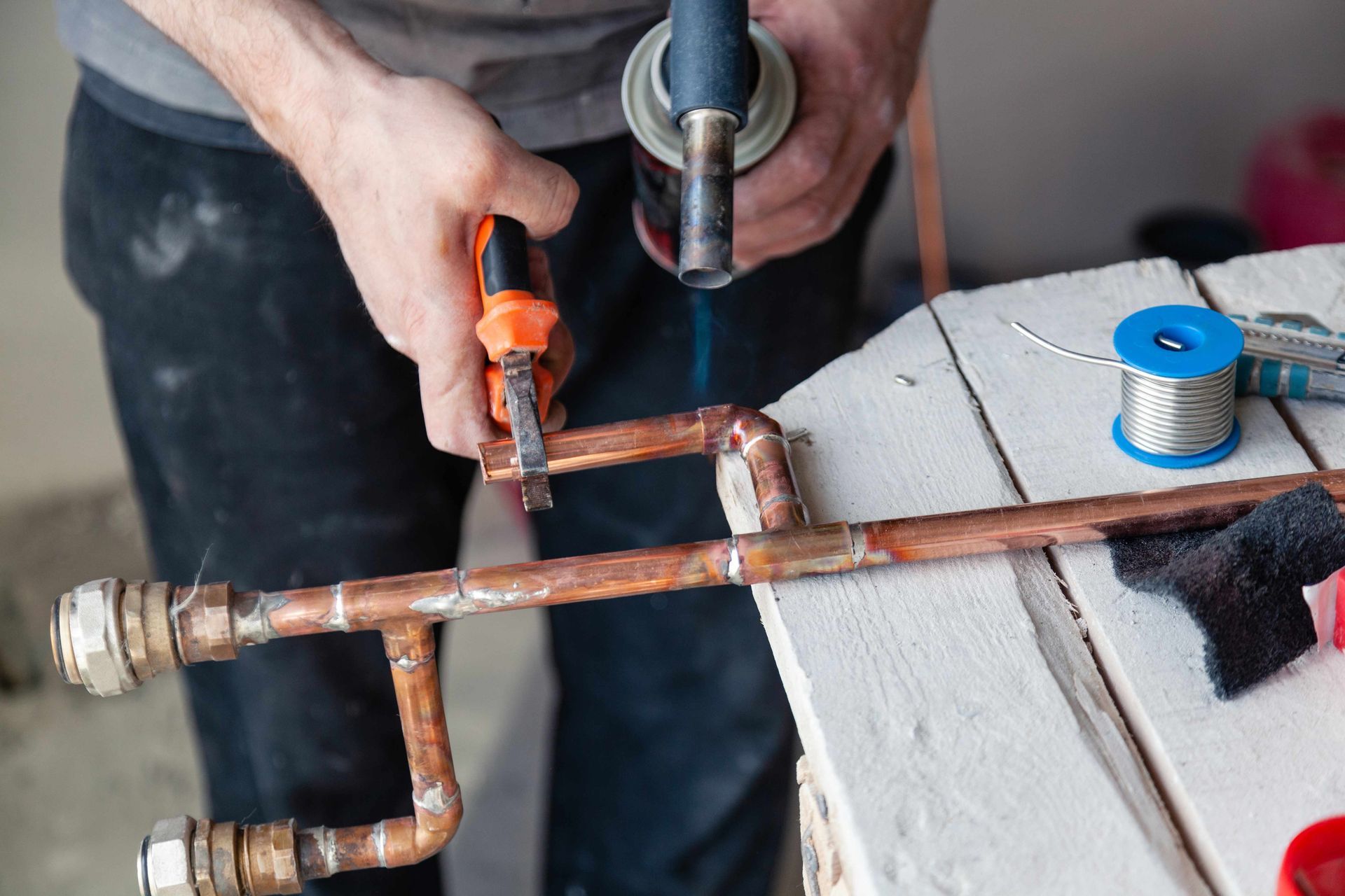 Person soldering copper pipes with a torch, using pliers on a workbench. Person soldering copper pipes with a torch, using pliers on a workbench.