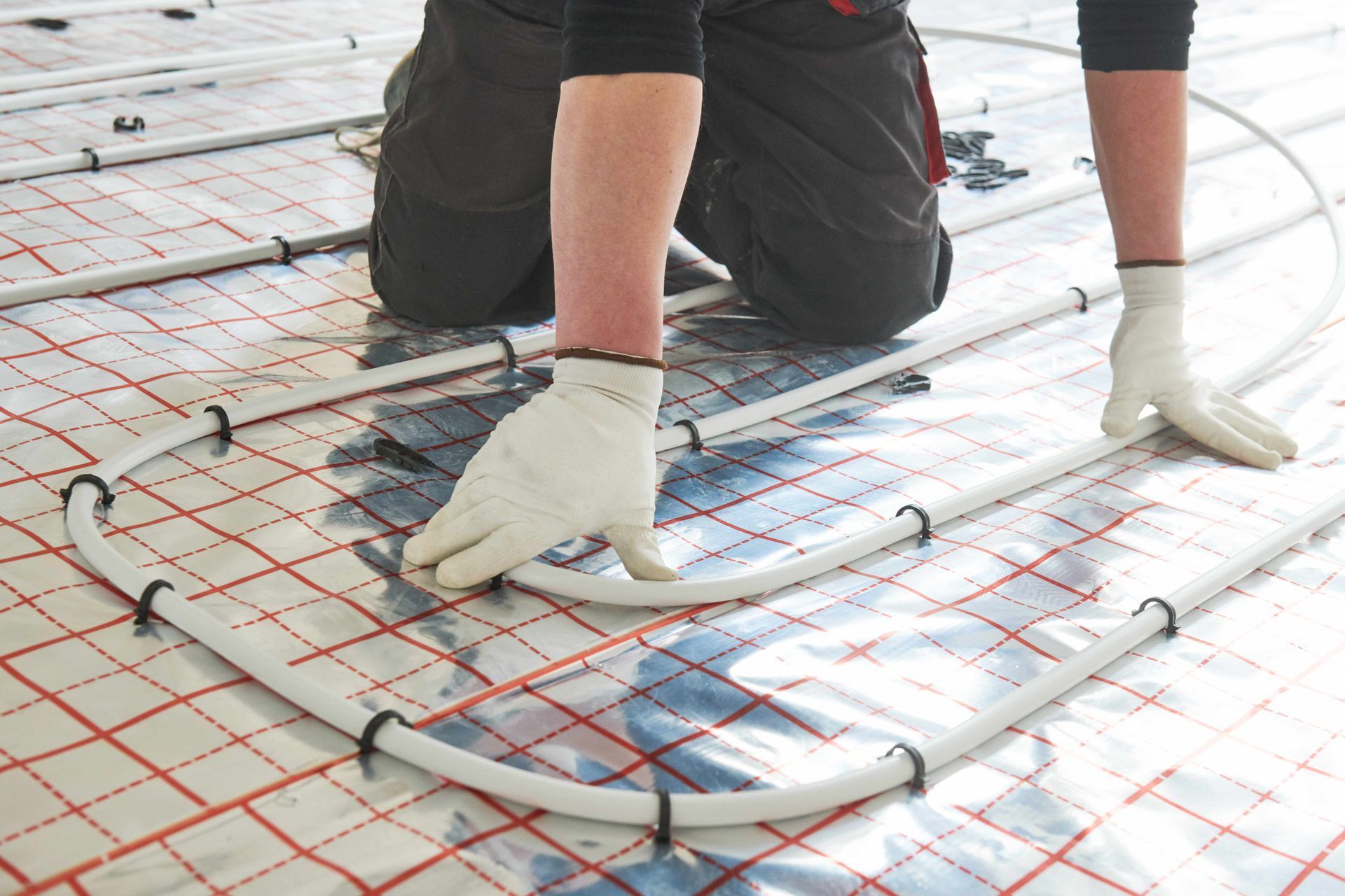Person installing radiant floor heating system, using white tubing and fasteners on a checkered surface.