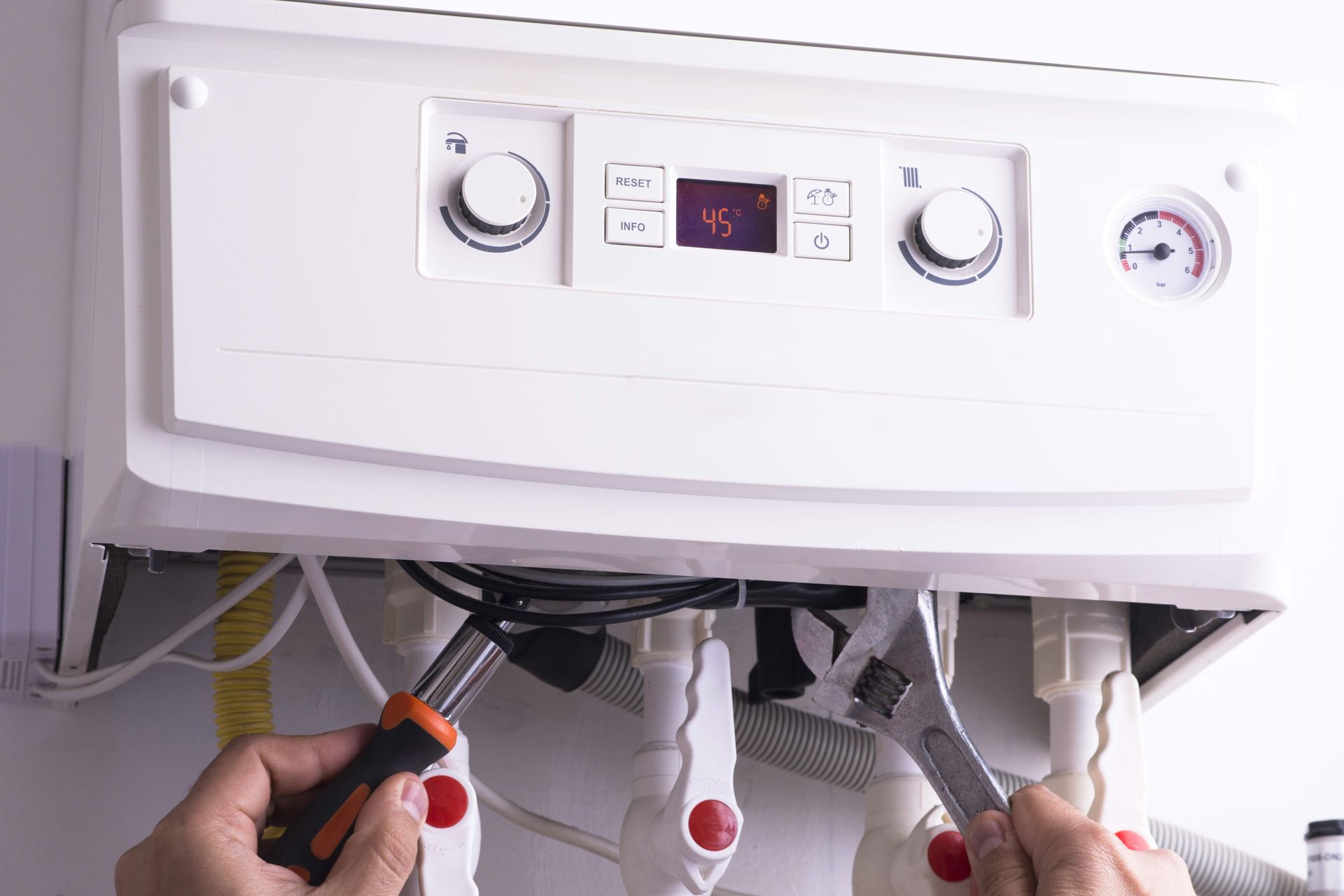 Person using a screwdriver and wrench to service a white boiler with gauges and control panel. Person using a screwdriver and wrench to service a white boiler with gauges and control panel.