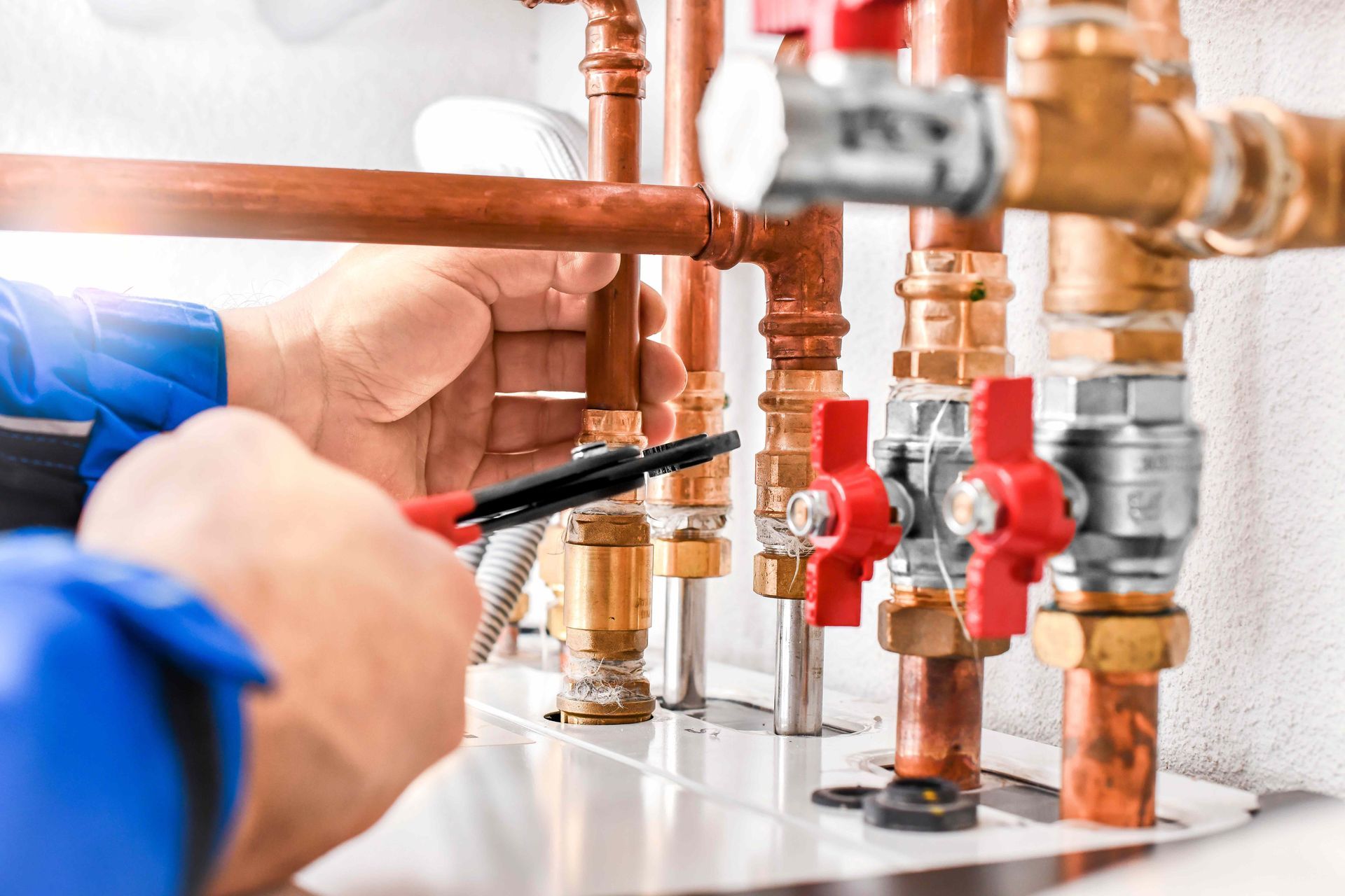 Plumber using a wrench to repair copper pipes with red and silver valves in a utility room.