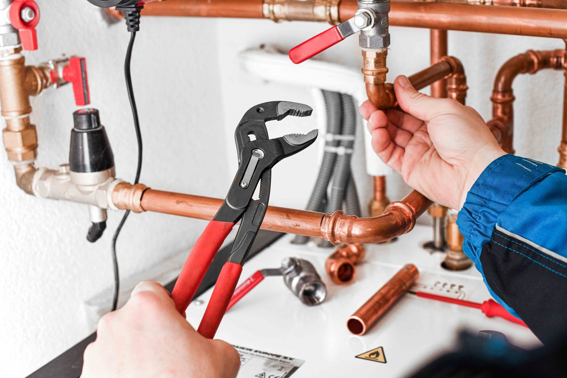 Plumber working on copper pipes with pliers in hand, near a white wall and other tools. Plumber working on copper pipes with pliers in hand, near a white wall and other tools.