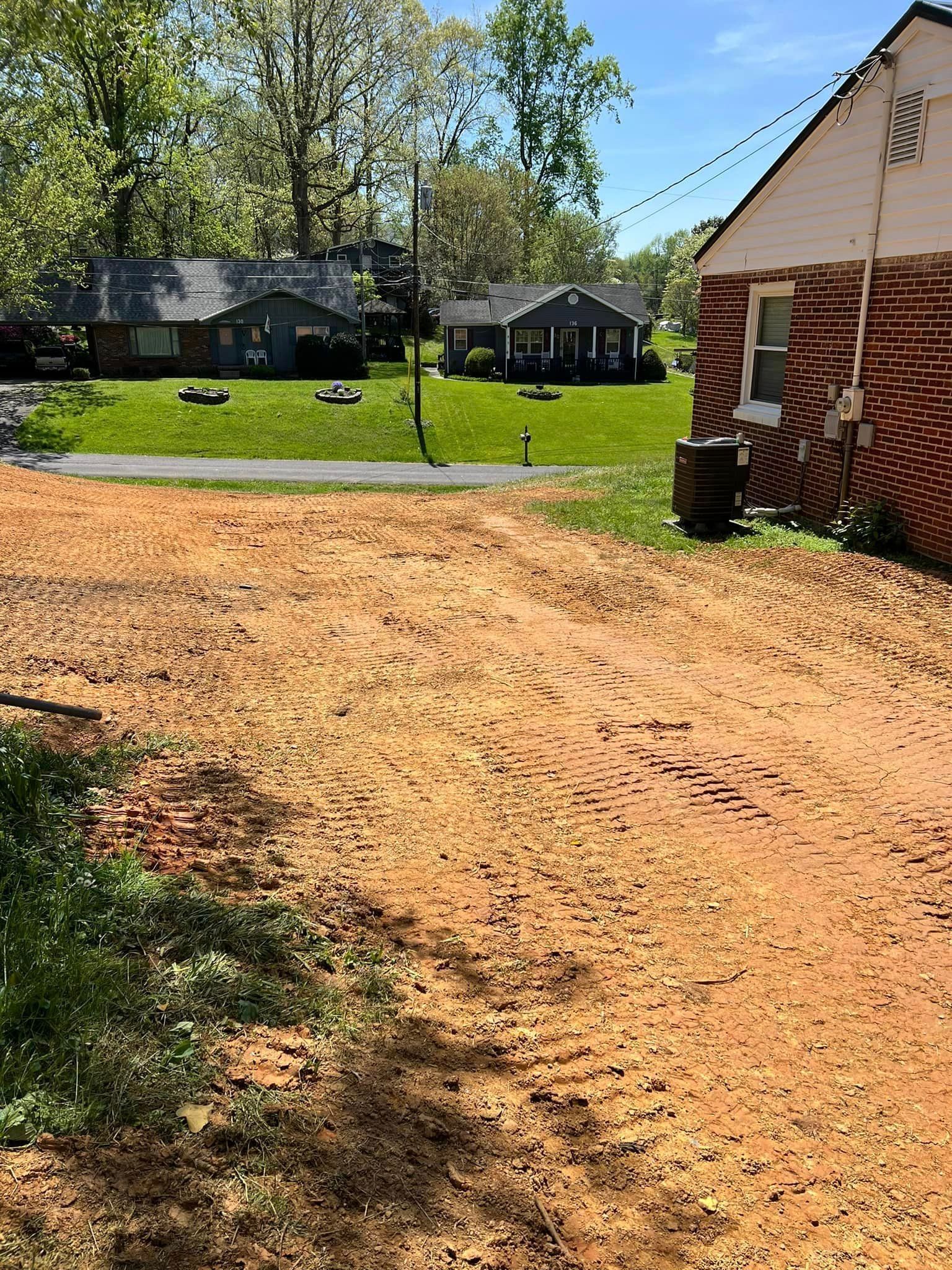 Dirt driveway in front of houses with green lawns and trees on a sunny day.