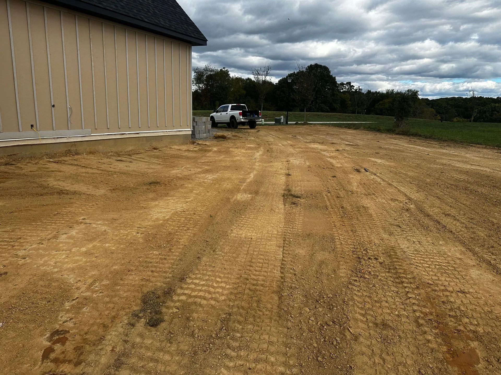 A gravel driveway in front of a tan building. A white truck is parked nearby. Cloudy sky.