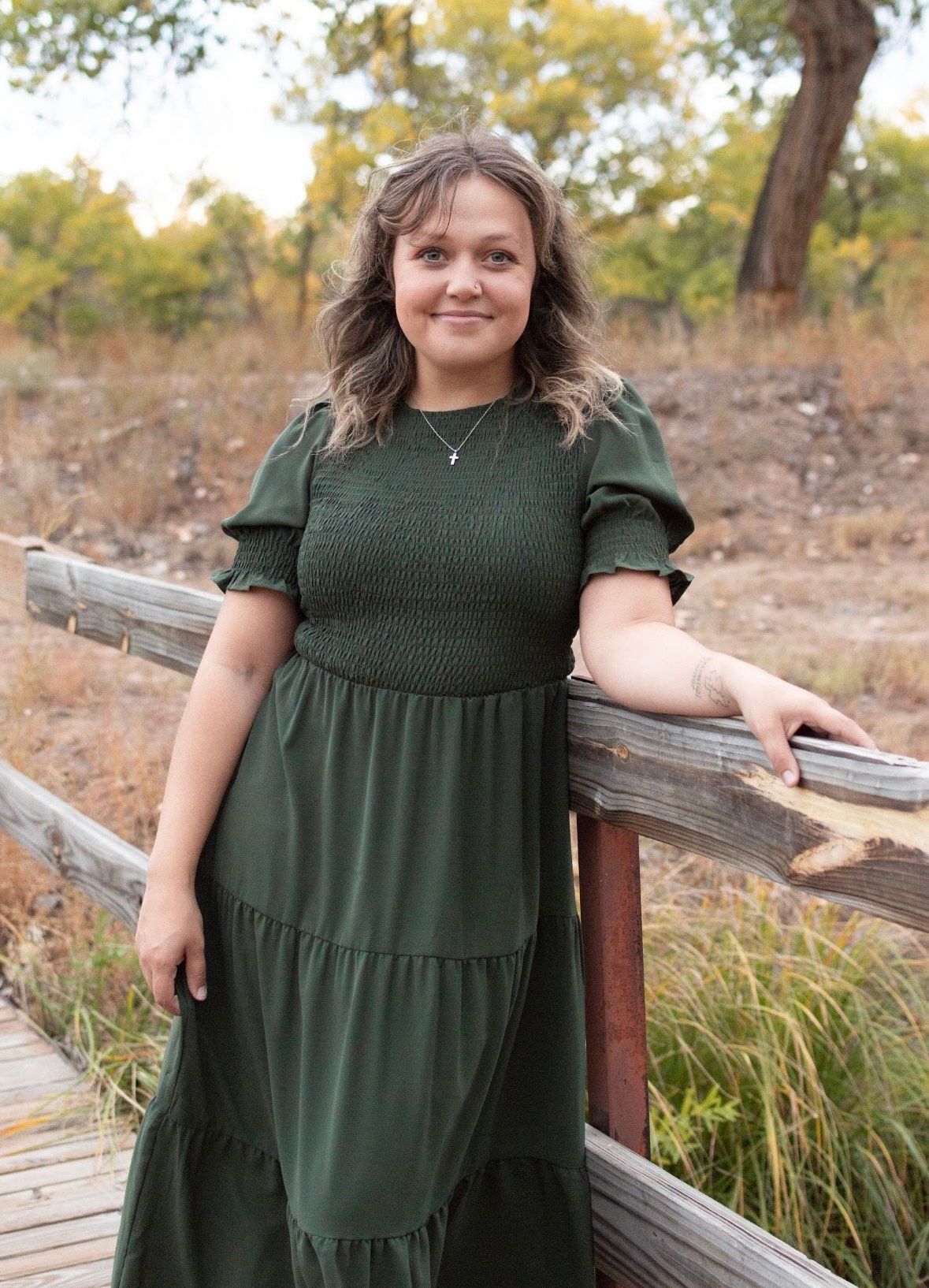 A woman is sitting on a wooden bridge with a hat on her lap.