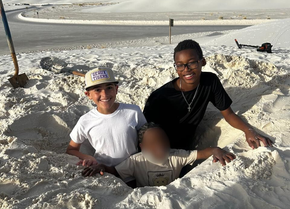 A woman in a red jacket with a fur hood is standing on a bridge in front of a city skyline.
