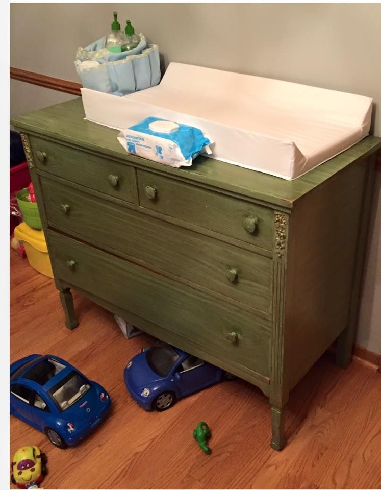 A green dresser with a changing table on top of it