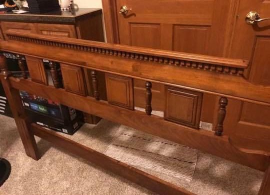 A wooden bed frame is sitting in a room next to a door.