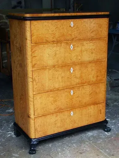 A wooden chest of drawers with black legs is sitting on a table.