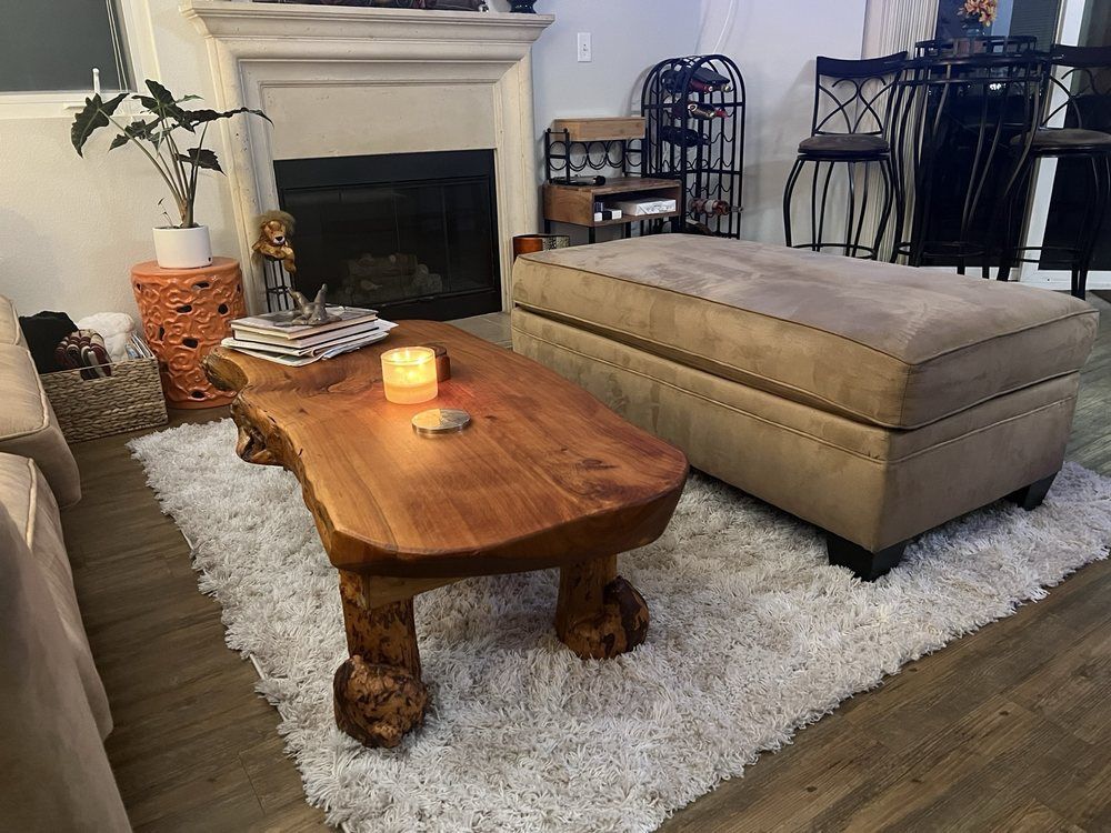 A living room with a coffee table , ottoman , and fireplace.