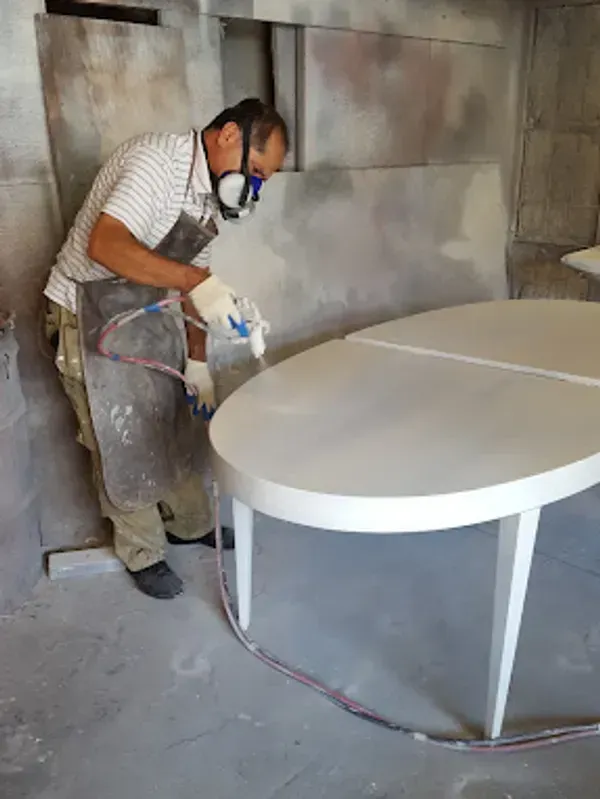 A man is spray painting a white table in a room.