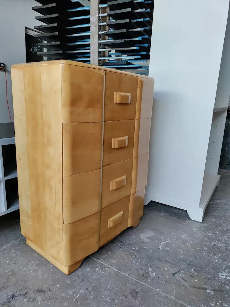 A wooden chest of drawers is sitting on a concrete floor in a room.
