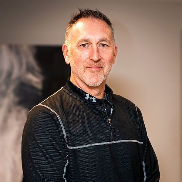 Middle-aged man with short hair and a trimmed beard, wearing a black zip-up shirt, looking at the camera.
