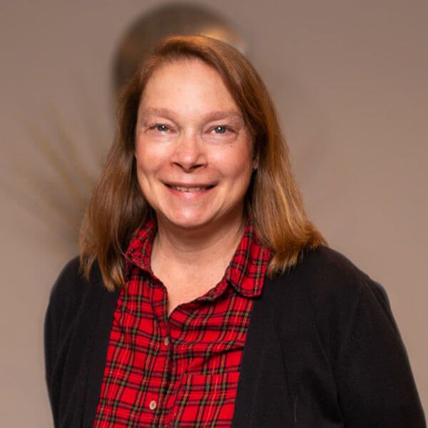 Woman smiles, wearing a red plaid shirt and black cardigan.