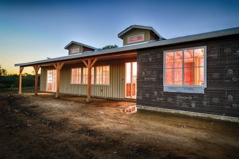 A wooden house with porch, windows glowing from inside, in twilight.