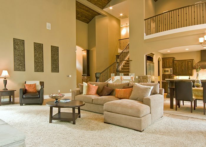 Spacious living room with beige walls, sofa, and dining area, with a staircase leading to a second-floor balcony.