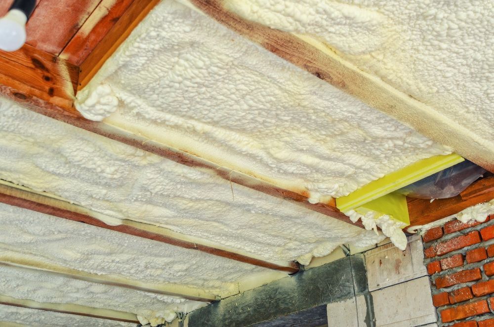 Ceiling insulation: Spray foam applied between wooden beams, against brick and concrete walls, creating a heat barrier.
