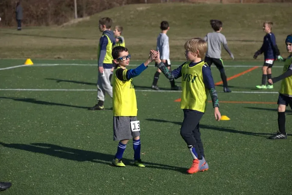 MSI soccer kids wearing yellow pinnies share a high five on the field during training session as teammates practice nearby.