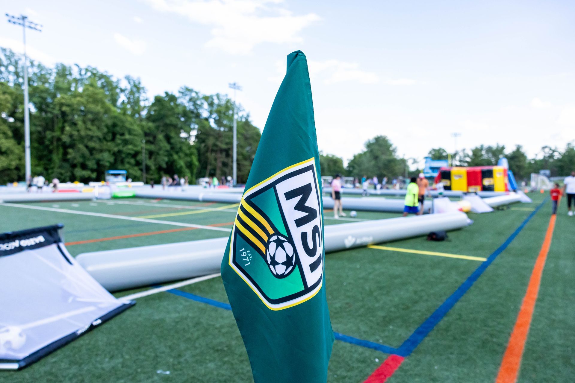 Close-up of an MSI corner-flag logo with inflatable mini-pitches and activities in the background.