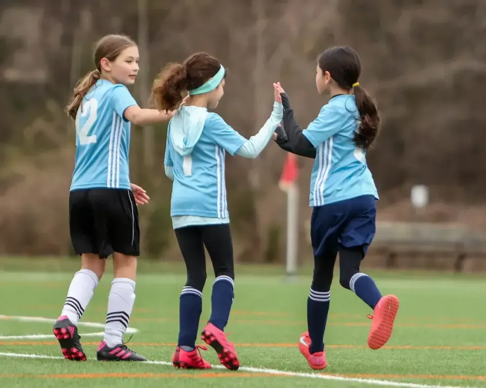 Three MSI youth players in light-blue Classic League jerseys high-five after a play, celebrating teamwork during a Recreation League match in Montgomery County, MD.