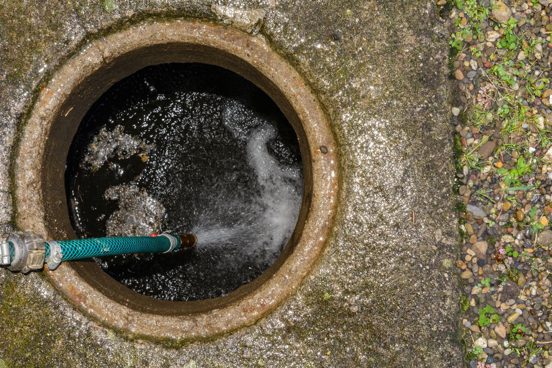A manhole cover with a green hose coming out of it.