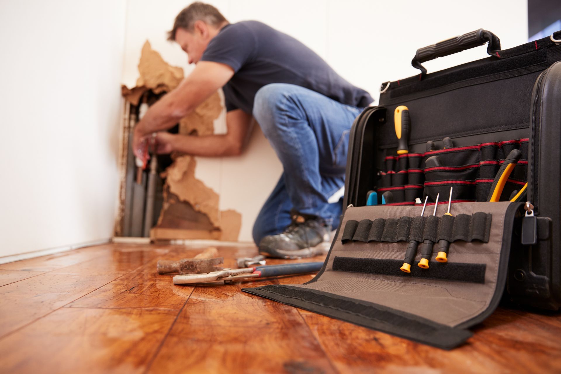 A man is working on a pipe in a room next to a tool bag.