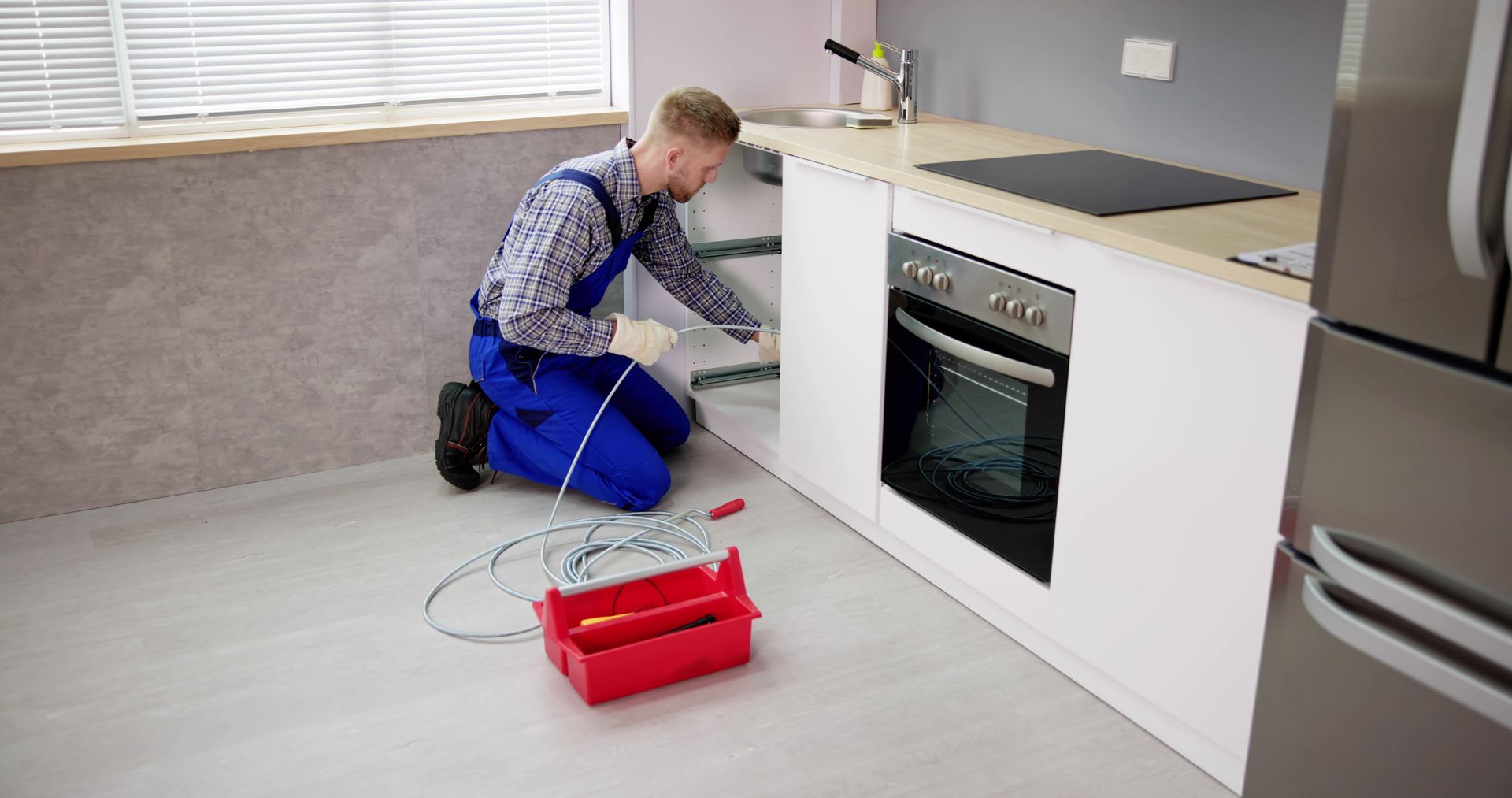 A man is kneeling down in a kitchen fixing a sink.