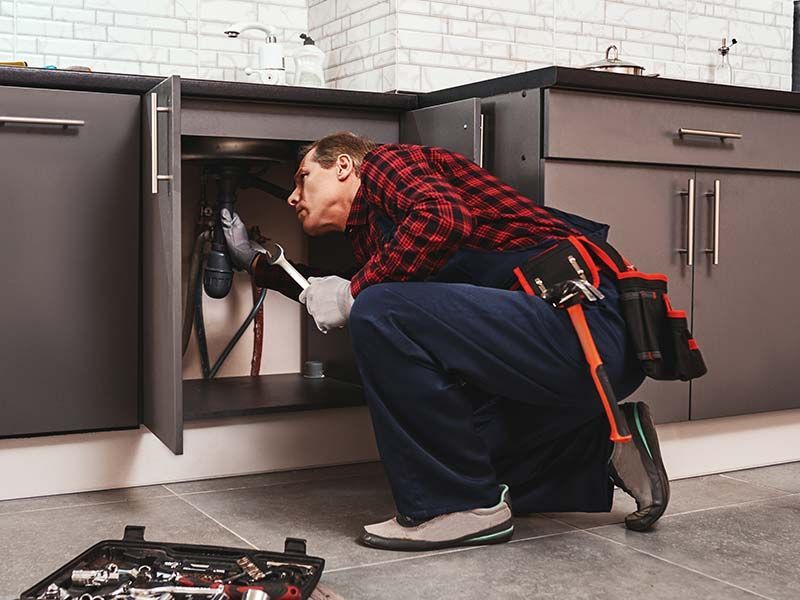 A man is fixing a sink in a kitchen.