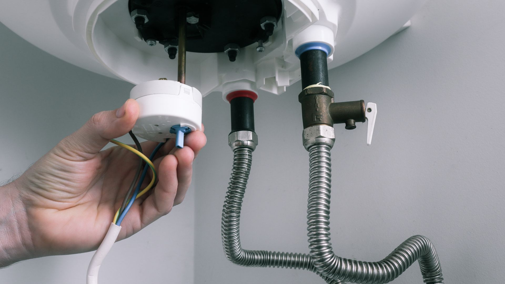 A person is fixing a water heater with a hose attached to it.