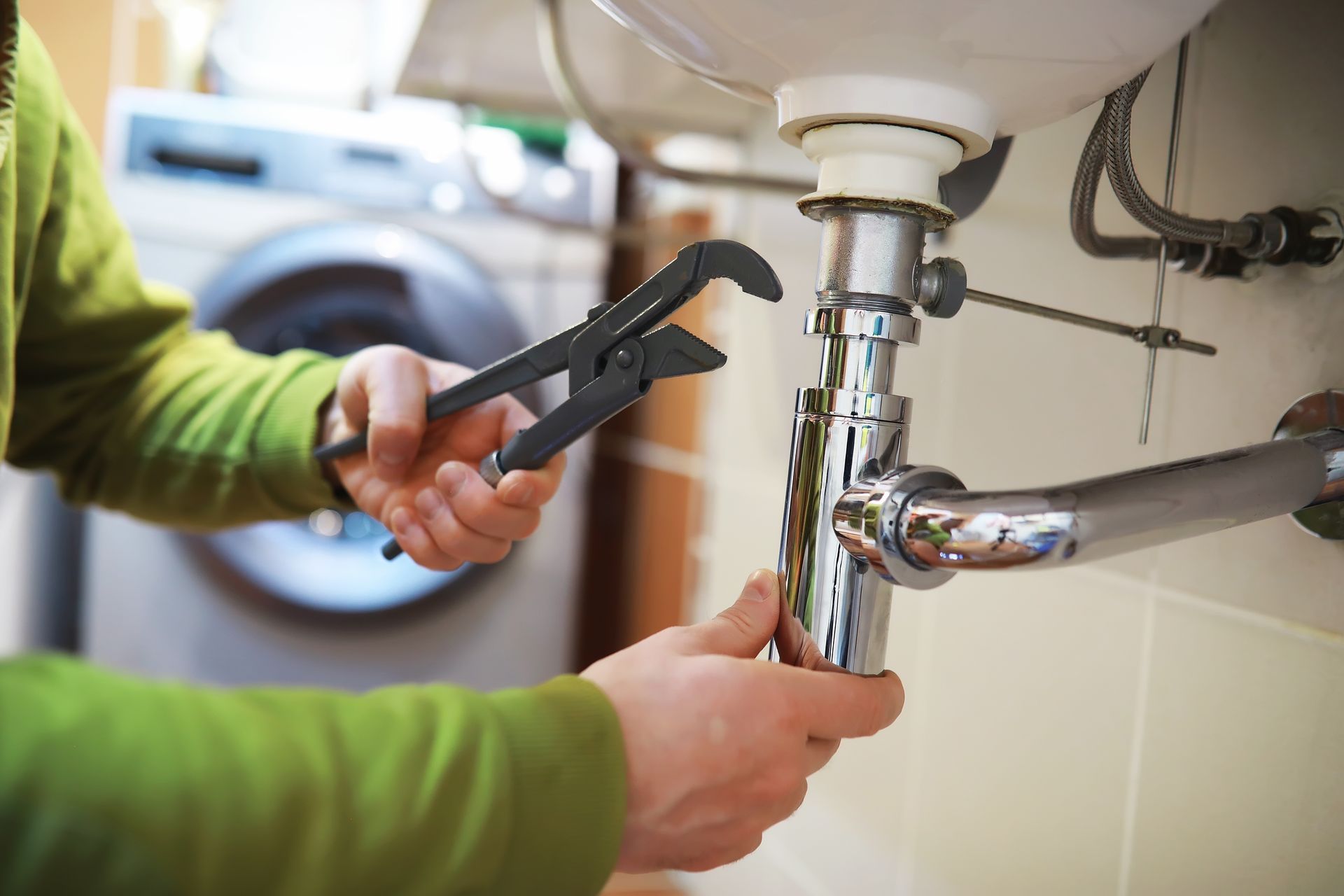 A plumber is fixing a sink with a wrench.