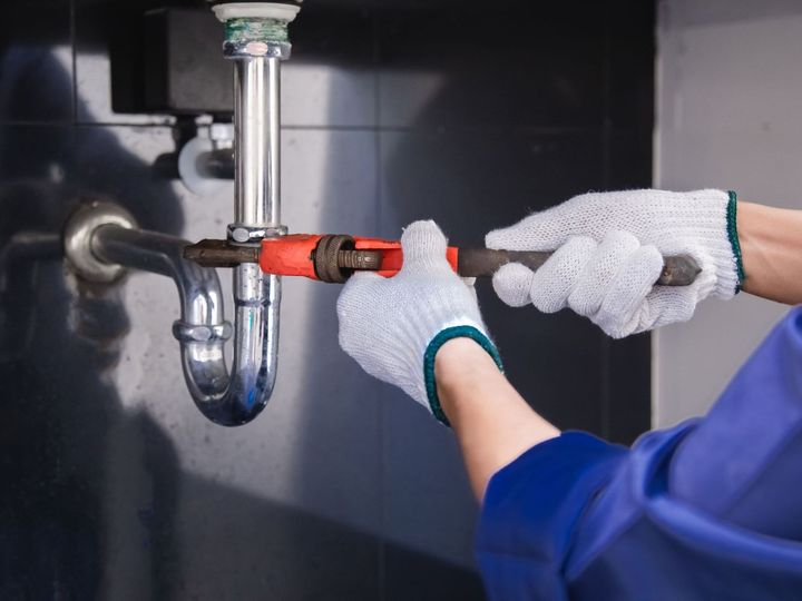 A plumber is fixing a sink pipe with a wrench.