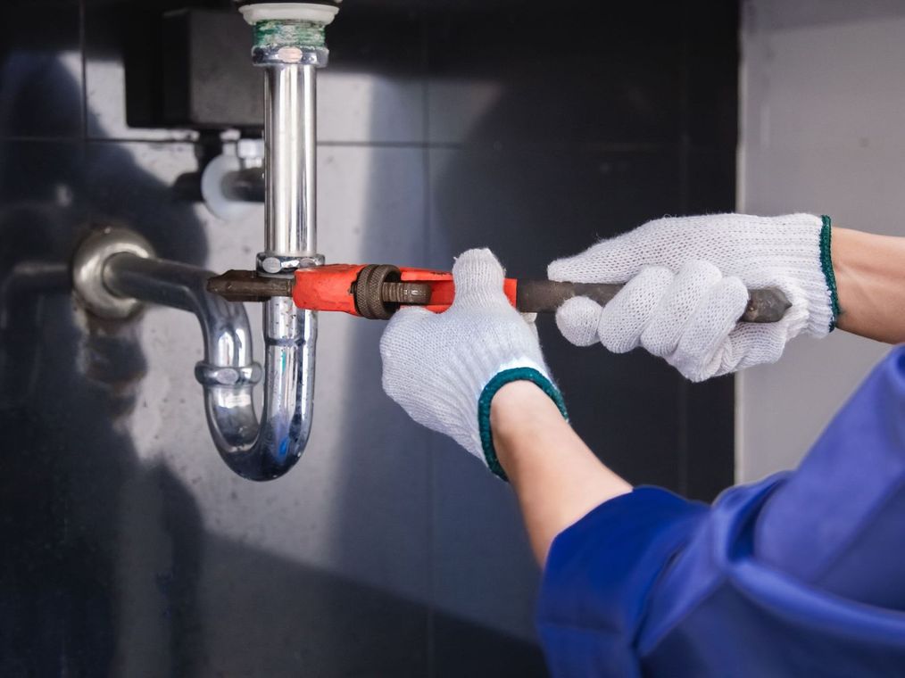 A plumber is fixing a sink pipe with a wrench.