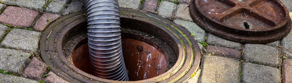 A hose is coming out of a manhole cover on a brick sidewalk.
