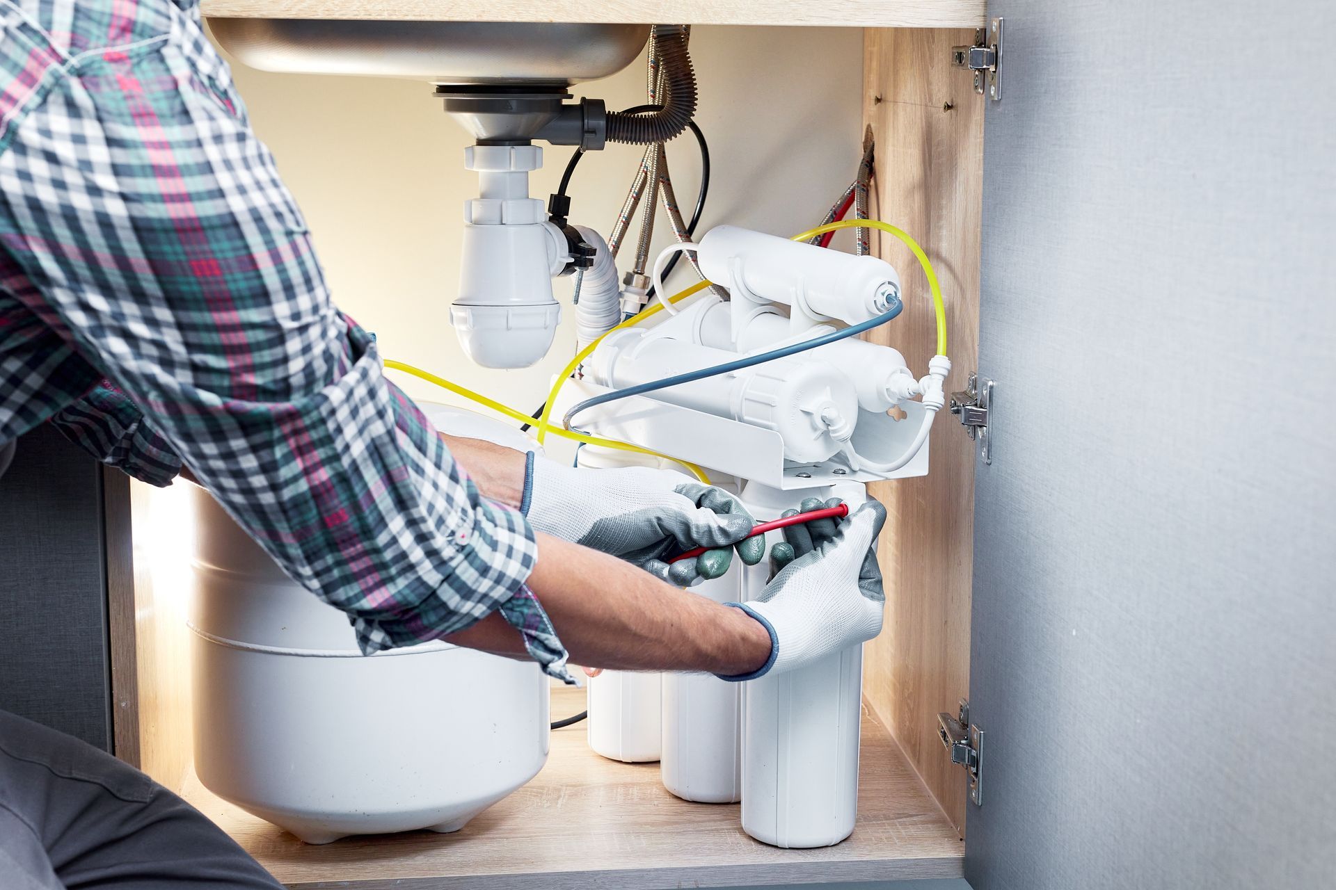 A man is fixing a water filter under a sink.