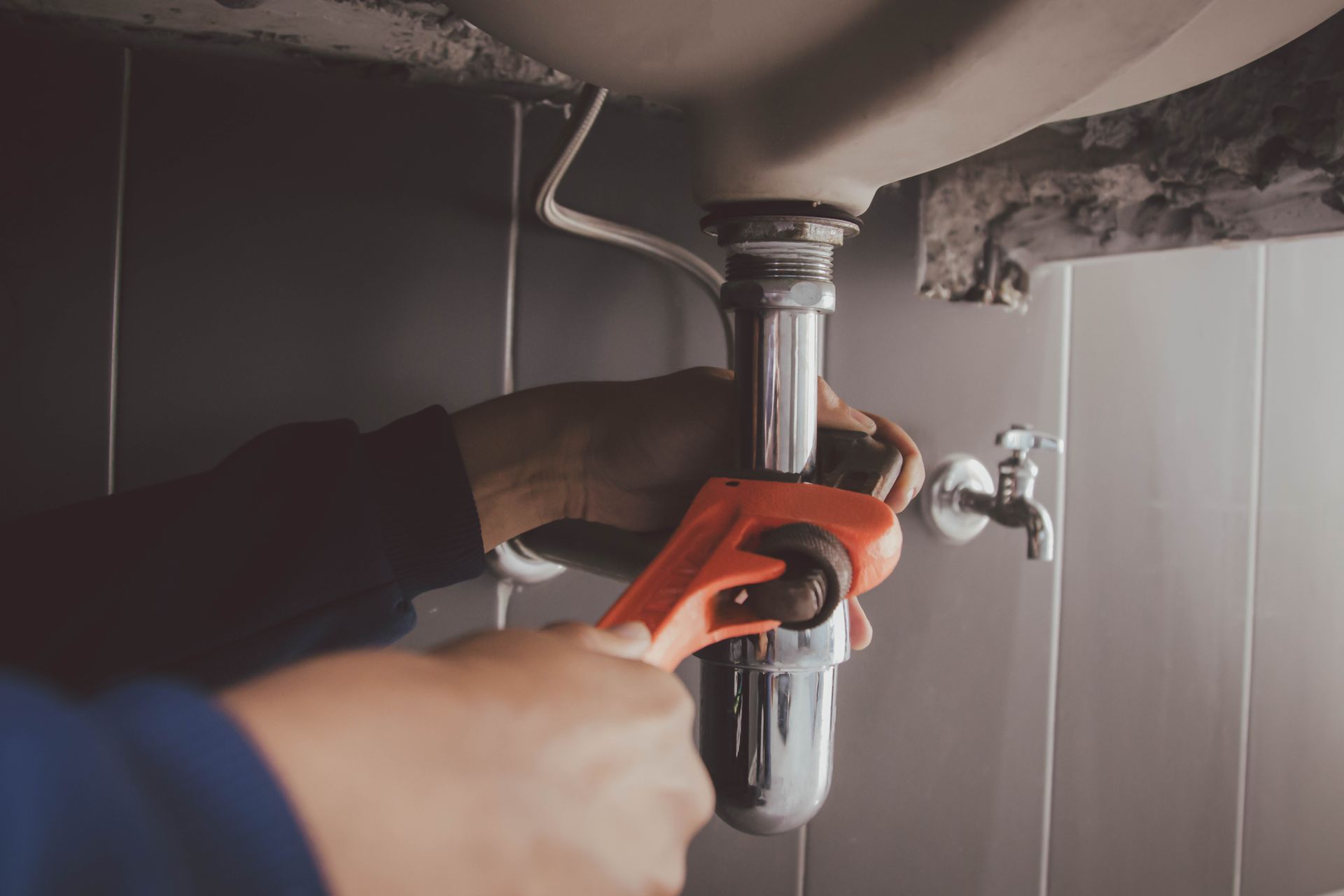 A plumber is fixing a sink with a wrench.