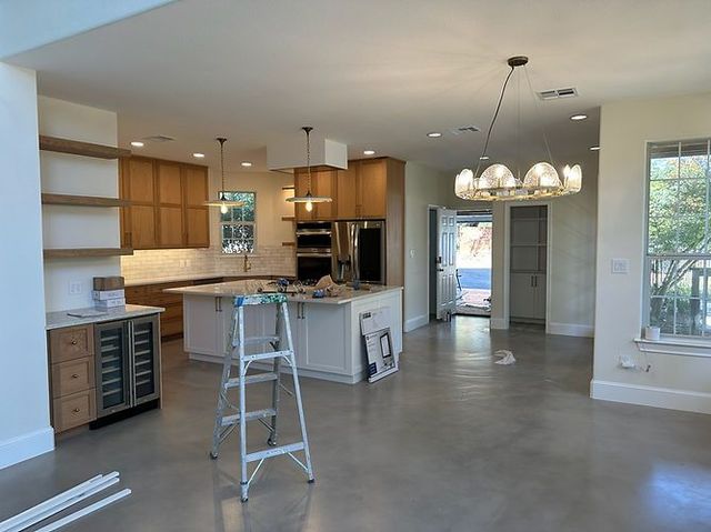 Empty modern kitchen with island, pendant lights, white cabinets, and a step stool on a concrete floor